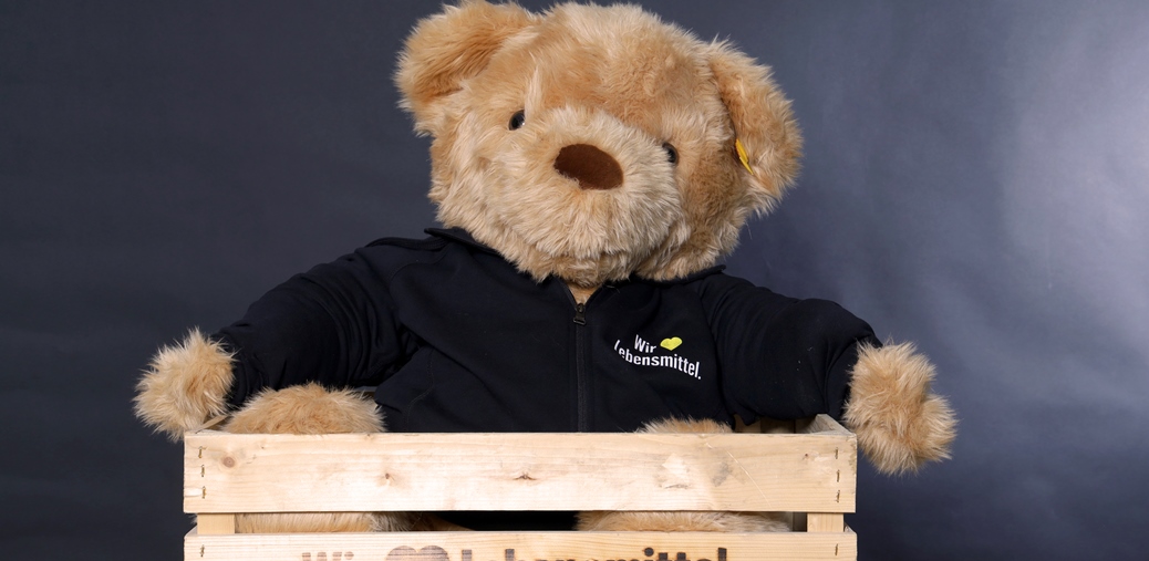 Teddybär mit Edeka T-Shirt in einer Obstkiste mit der Aufschrift "Wir lieben Lebensmittel"