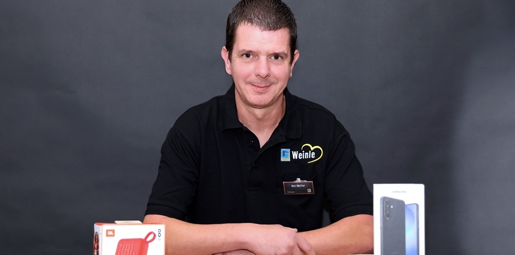 Mitarbeiterfoto im Edeka T-Shirt mit Mobile-Produkteverpackungen im Vordergrund