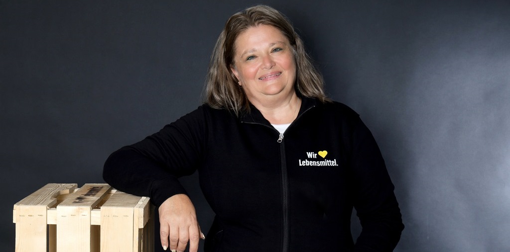 Mitarbeiterin im Edeka T-Shirt die sich an eine leere Obstkiste anlehnt